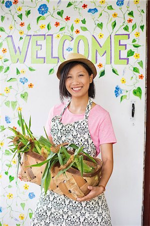 symbol for female - Working on an organic farm. A young Asian woman by the Welcome sign with a large basket of vegetables, freshly picked. Stock Photo - Premium Royalty-Free, Code: 6118-07203874