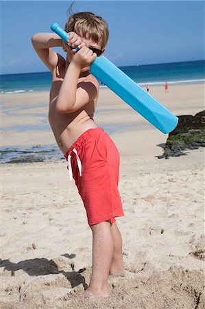 A boy standing on the sand with a small blue cricket bat in his hands. Stock Photo - Premium Royalty-Free, Code: 6118-07203838