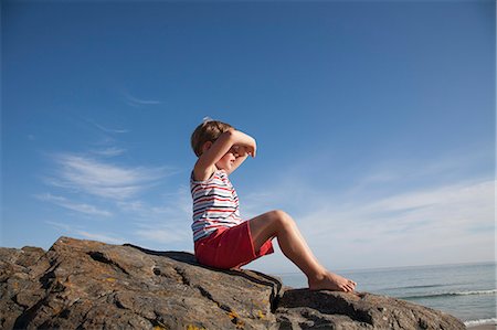 A child seated on the rocks looking out to sea. Stock Photo - Premium Royalty-Free, Code: 6118-07203839