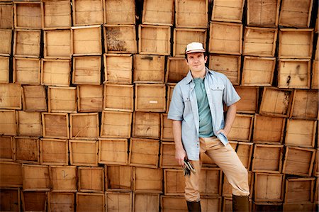 A farmer standing in front of a wall of stacked wooden crates for produce. Stock Photo - Premium Royalty-Free, Code: 6118-07203924