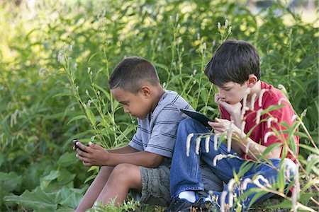 simsearch:6118-08243810,k - Two boys sitting in a field, one on a smart phone and one using a digital tablet. Stock Photo - Premium Royalty-Free, Code: 6118-07235143