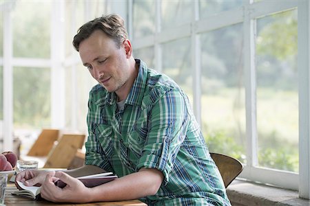 A man sitting at a table reading a book. Stock Photo - Premium Royalty-Free, Code: 6118-07235221