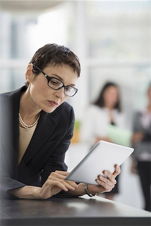 simsearch:6118-07351367,k - An office interior. A woman in a black jacket using a digital tablet. Photographie de stock - Premium Libres de Droits, Code: 6118-07351356