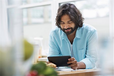 An office or apartment interior in New York City. A bearded man in a turquoise shirt using a digital tablet. Stock Photo - Premium Royalty-Free, Code: 6118-07351377