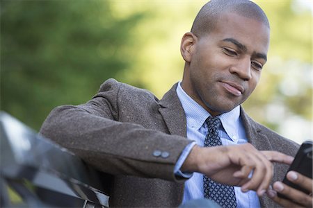 Business people in the city. Keeping in touch on the move. A man seated on a bench. Checking his cell phone. Stock Photo - Premium Royalty-Free, Code: 6118-07351482