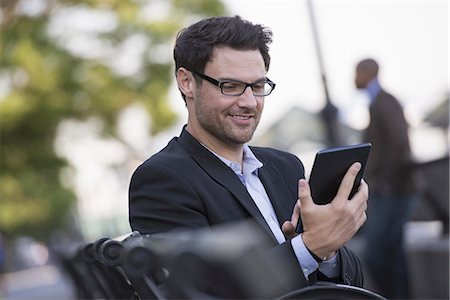 simsearch:6118-07440408,k - Business people in the city. Keeping in touch on the move. A man seated on a bench, using a digital tablet. Stock Photo - Premium Royalty-Free, Code: 6118-07351484