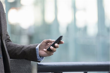 people looking phones - Business people in the city. Keeping in touch on the move. A man standing outdoors checking his cell phone. Stock Photo - Premium Royalty-Free, Code: 6118-07351494