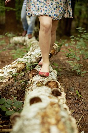 Two people walking along a fallen tree trunk in the woods. Stock Photo - Premium Royalty-Free, Code: 6118-07351683