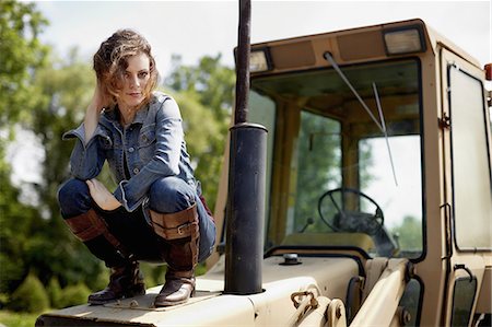 simsearch:6118-07354445,k - A young woman in denim jacket and boots on the hood of a tractor. Stock Photo - Premium Royalty-Free, Code: 6118-07351635