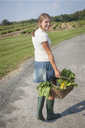 A girl in boots on a farm carrying a basket full of fresh produce. Stock Photo - Premium Royalty-Free, Code: 6118-07351901