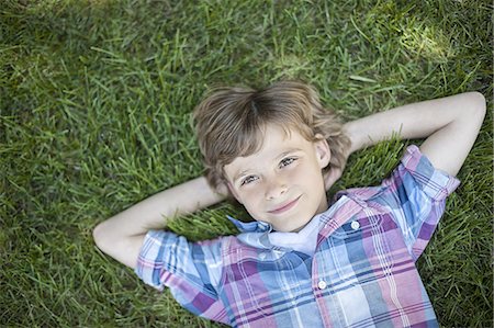 A boy lying on the grass, hands behind his head. Stock Photo - Premium Royalty-Free, Code: 6118-07352166