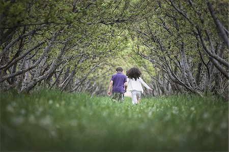 Two children running along a natural woodland tree branch tunnel. Stock Photo - Premium Royalty-Free, Code: 6118-07352208