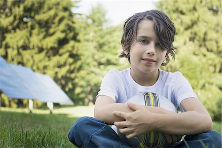 solar panel usa - A boy holding a football, sitting on the grass. Solar panels. Stock Photo - Premium Royalty-Free, Code: 6118-07352463