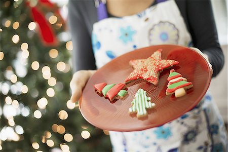 A woman wearing an apron holding a plate of organic decorated Christmas cookies. Stock Photo - Premium Royalty-Free, Code: 6118-07352968