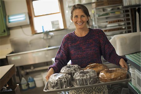 simsearch:6118-07354445,k - A woman in a kitchen carrying a tray of iced fresh baked cakes. Stock Photo - Premium Royalty-Free, Code: 6118-07353348