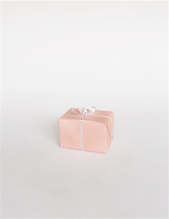 A small boxed gift wrapped in pink paper with a ribbon, on white background Stock Photo - Premium Royalty-Free, Code: 6118-07353302