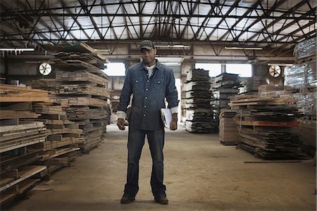 A heap of recycled reclaimed timber planks of wood. Environmentally responsible reclamation in a timber yard. A man in work overalls with a clipboard. Stock Photo - Premium Royalty-Free, Code: 6118-07353400