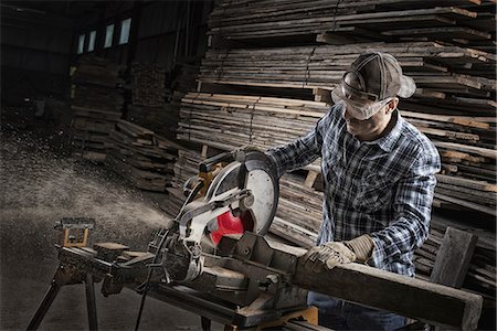 piles of work - A reclaimed lumber workshop. A man in protective eye goggles using a circular saw to cut timber. Photographie de stock - Premium Libres de Droits, Code: 6118-07353420