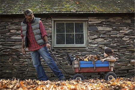 simsearch:6118-07353446,k - A man in a padded jacket pulling a garden cart with a child sitting among the dried autumn leaves. A traditional stone building. Stock Photo - Premium Royalty-Free, Code: 6118-07353430