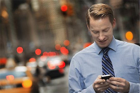 equipment - A man in a suit checking his cell phone, standing on a city sidewalk at dusk. Stock Photo - Premium Royalty-Free, Code: 6118-07353617