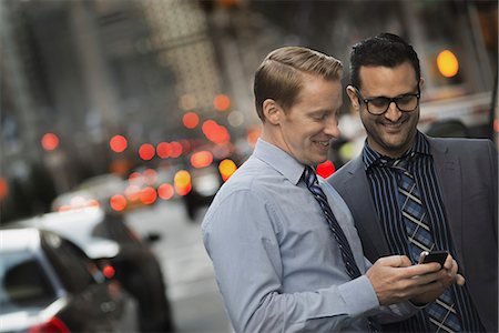 simsearch:6118-07440408,k - Two men standing together looking at a cell phone display on a busy street at dusk. Stock Photo - Premium Royalty-Free, Code: 6118-07353614