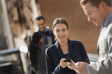 simsearch:6118-07440408,k - Three people standing on the sidewalk in the city, checking their phones. Two men and a woman. Stock Photo - Premium Royalty-Free, Code: 6118-07353631