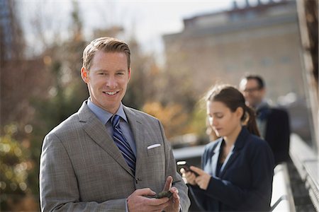 simsearch:6118-07440408,k - Three people standing on the sidewalk in the city, checking their phones. Two men and a woman. Stock Photo - Premium Royalty-Free, Code: 6118-07353632