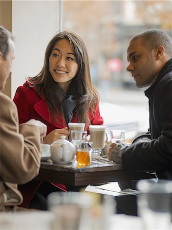 City life. A group of people on the go. Three people in a coffee shop sitting at a table, and talking to each other. Stock Photo - Premium Royalty-Free, Code: 6118-07353716