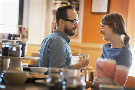 A couple sitting in a coffeeshop smiling and talking over a cup of coffee. Stock Photo - Premium Royalty-Free, Code: 6118-07353726