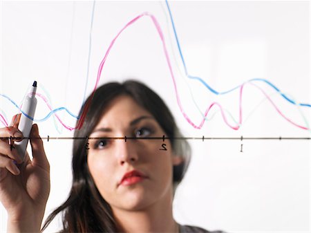A young woman drawing coloured graph lines across a graph illustration, on a see through surface. Stock Photo - Premium Royalty-Free, Code: 6118-07354229