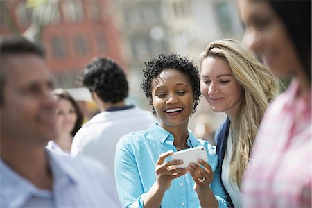surprise - People outdoors in the city in spring time. New York City. A group of men and women, two women looking at a cell phone. Stock Photo - Premium Royalty-Free, Code: 6118-07354351