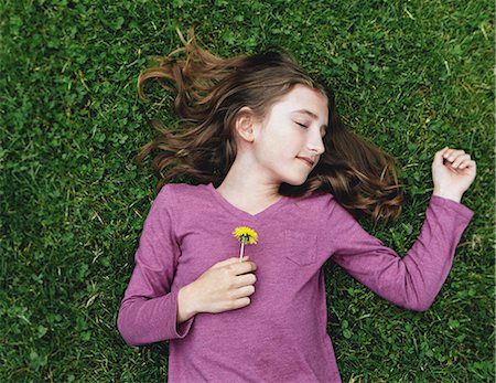 A ten year old girl lying on the grass with her eyes closed, holding a dandelion flower. Foto de stock - Sin royalties Premium, Código: 6118-07354309