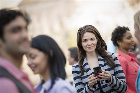 funny group - People outdoors in the city in spring time. New York City park. A young woman holding a mobile phone, and looking up at the camera. Stock Photo - Premium Royalty-Free, Code: 6118-07354320