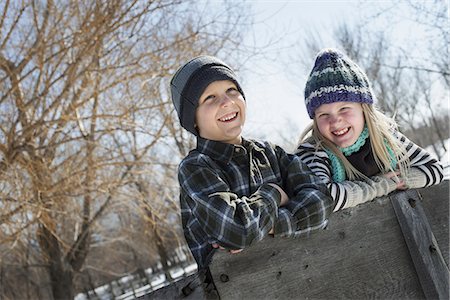 simsearch:6118-07354445,k - Winter scenery with snow on the ground. Two children in knitted hats leaning on a fence. Stock Photo - Premium Royalty-Free, Code: 6118-07354454
