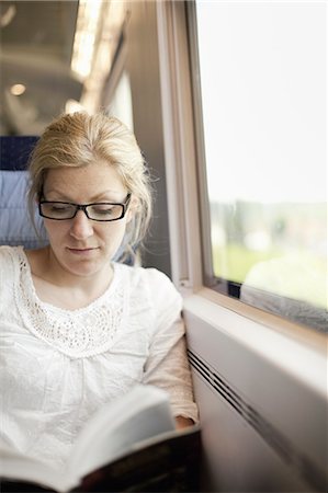 passenger (female) - A woman sitting by a train window, reading a book. Stock Photo - Premium Royalty-Free, Code: 6118-07354490