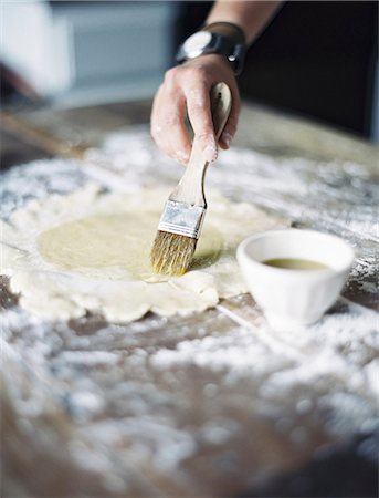 A domestic kitchen. A woman preparing a meal. Rolling out pastry on a table top and brushing it with egg wash. Stock Photo - Premium Royalty-Free, Code: 6118-07354419