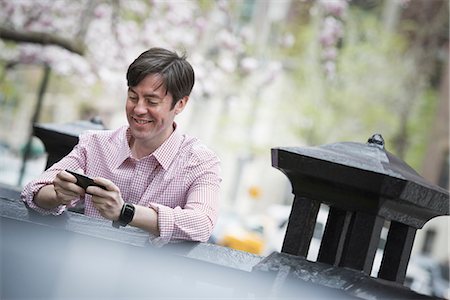 simsearch:6118-07122740,k - City life in spring. A man sitting outdoors in a city park. Looking down at his smart phone and smiling. Photographie de stock - Premium Libres de Droits, Code: 6118-07354574