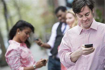 simsearch:6118-07121866,k - City life in spring. Young people outdoors in a city park. Three people checking, looking down at their cell phones. Stock Photo - Premium Royalty-Free, Code: 6118-07354582