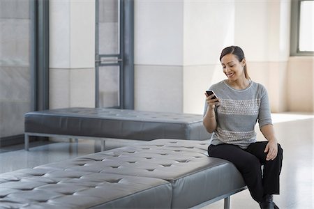 simsearch:6118-07354515,k - Urban Lifestyle. A young woman sitting on a seat in a building, using her mobile phone. Stock Photo - Premium Royalty-Free, Code: 6118-07354519