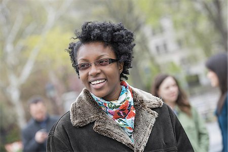 A group of people in a city park. A young woman in a coat with a large collar, smiling and looking at the camera. Stock Photo - Premium Royalty-Free, Code: 6118-07354640