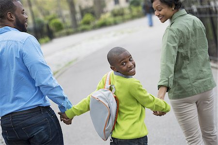 A New York city park in the spring. A boy with a bookbag, holding hands with his mother and father. Stock Photo - Premium Royalty-Free, Code: 6118-07354683