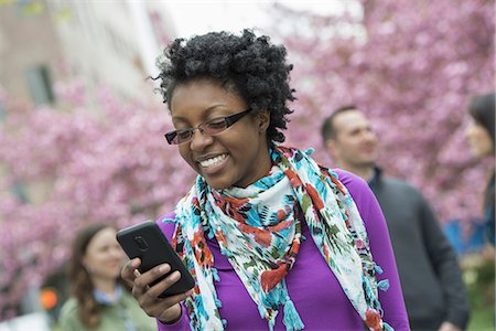 simsearch:6118-07122740,k - A group of people under the cherry blossom trees in the park. A young woman smiling and checking her phone. Photographie de stock - Premium Libres de Droits, Code: 6118-07354634
