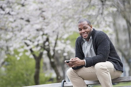 simsearch:6118-07203820,k - Outdoors in the city in spring. An urban lifestyle. A man sitting on a bench in the park, holding a phone. Stock Photo - Premium Royalty-Free, Code: 6118-07354748