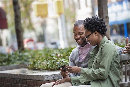 simsearch:6118-07354682,k - Outdoors in the city in spring. An urban lifestyle. A couple sitting side by side and looking at a phone screen. Stock Photo - Premium Royalty-Free, Code: 6118-07354731