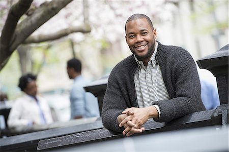 expression - Outdoors in the city in spring. An urban lifestyle. A man seated at a table, and two people in the background. Stock Photo - Premium Royalty-Free, Code: 6118-07354739