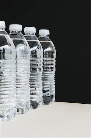 simsearch:6118-07354031,k - Row of clear, plastic water bottles filled with filtered water in a row. on a black background. Stock Photo - Premium Royalty-Free, Code: 6118-07440240