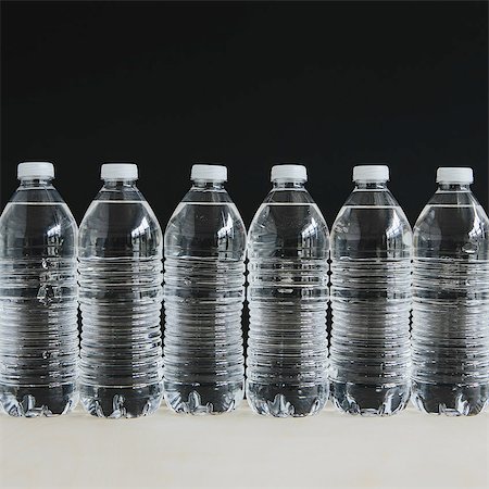 simsearch:6118-07354031,k - Row of clear, plastic water bottles filled with filtered water in a row, on a black background. Stock Photo - Premium Royalty-Free, Code: 6118-07440239
