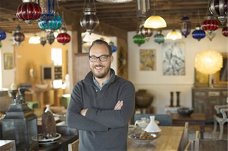 A man standing in a shop full of antique and decorative objects. Antique shop displays. Lighting, glass shades and furniture. Stock Photo - Premium Royalty-Free, Code: 6118-07440354