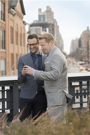 simsearch:6118-07440408,k - Two men in formal business clothes, standing side by side, looking at a cell phone screen or mobile phone. Stock Photo - Premium Royalty-Free, Code: 6118-07440409