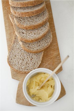 A wooden breadboard with a sliced brown loaf laid out. A dish of butter with a wooden butter knife. Photographie de stock - Premium Libres de Droits, Code: 6118-07440872